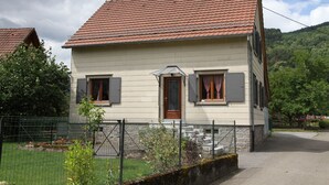 A two-story house with a red-tiled roof, a front door, and a small garden area with a fence. - Detached house in Metzeral for 8 to 10 people, in the Munster valley (Metzeral)