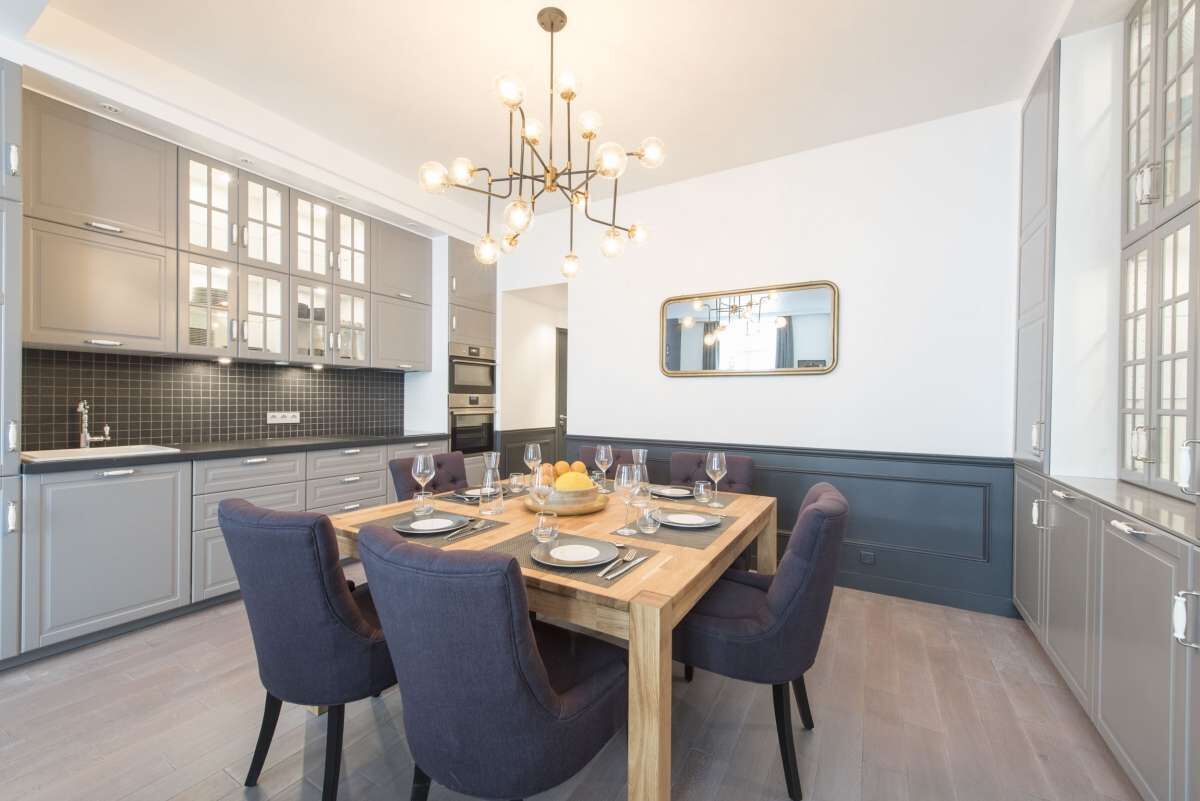 Une cuisine moderne avec des meubles de couleur grise, une table à manger en bois pour six personnes et un lustre.
