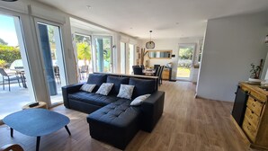 Uma sala de estar moderna com um sofá modular preto, uma mesa de centro redonda e um espaço de jantar com mesa e cadeiras de madeira.