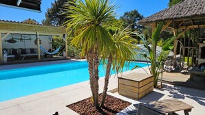 Piscina com deck de madeira, palmeiras e estrutura coberta de palha.