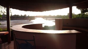 Un espacio de estar al aire libre techado con un banco de madera curvo y vistas a una playa y un cuerpo de agua.
