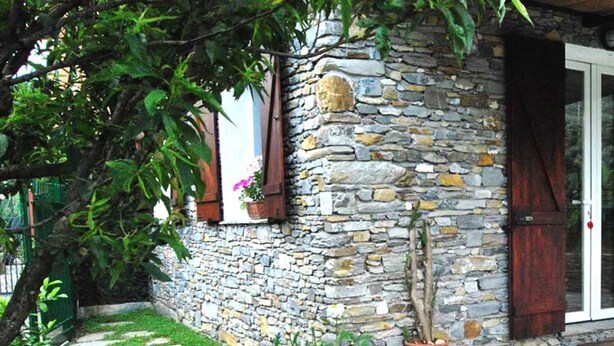 A stone building with a stone pathway leading to a door, surrounded by greenery and flowers. - The old mill (Rapallo)