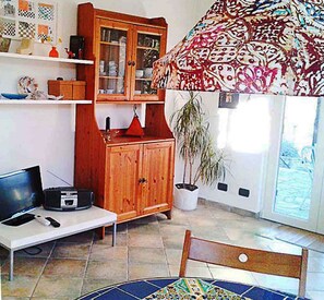 A living room with a TV, wooden cabinet, potted plant, and a patterned sofa.