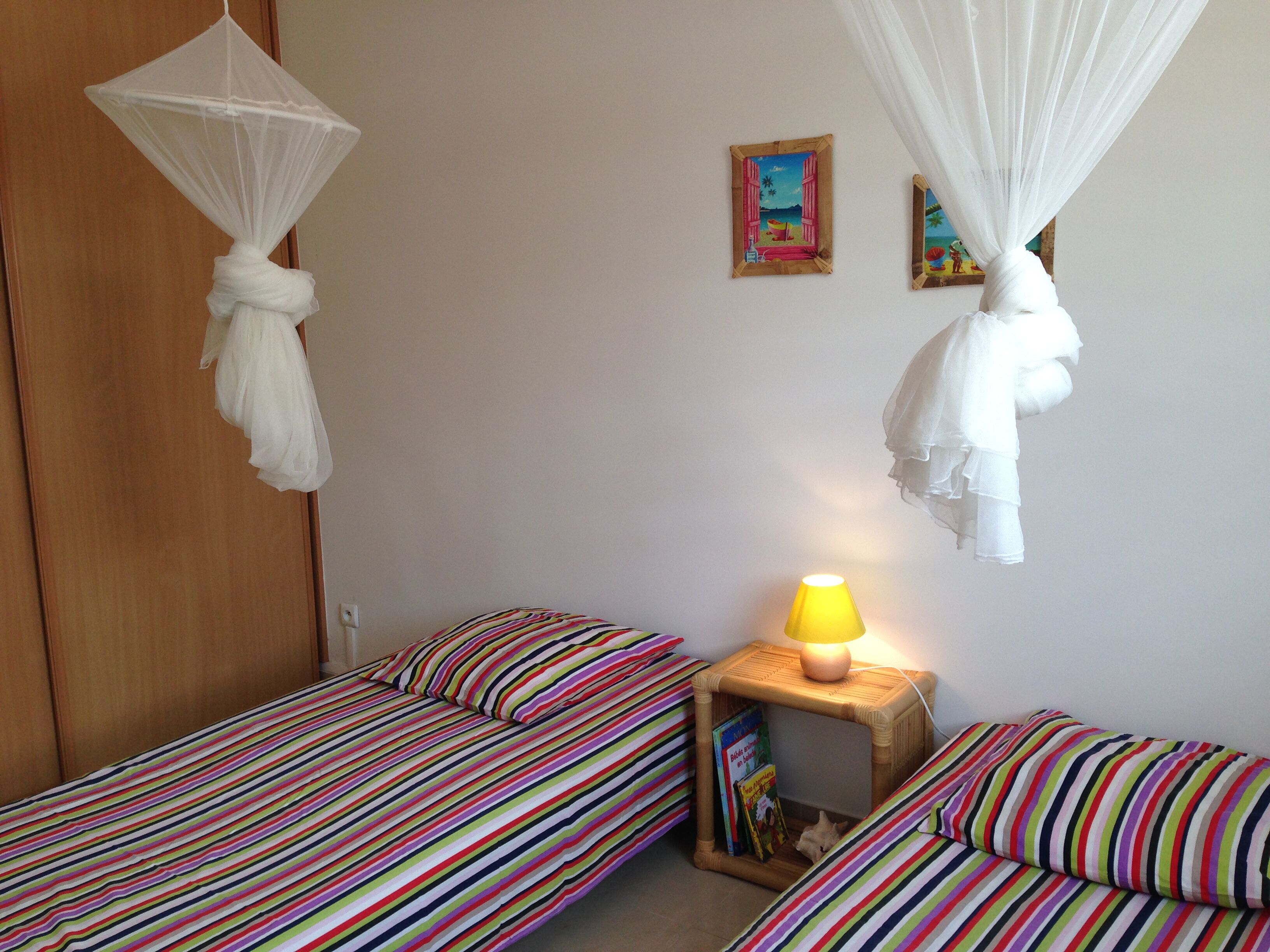 Une chambre avec deux lits, chacun doté de draps à rayures, une table de chevet avec une lampe et une petite étagère avec des livres.