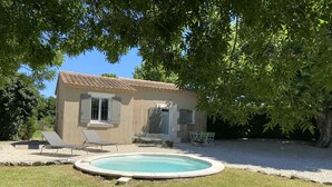 Une petite maison avec une piscine, entourée d’une pelouse et d’arbres.