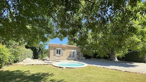 Une petite maison avec une piscine, entourée d’une pelouse bien entretenue et d’arbres.