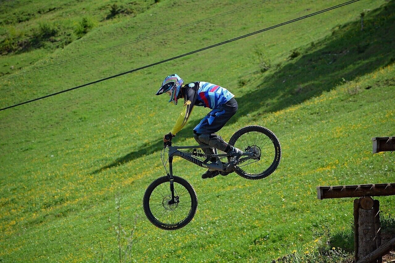 A person on a mountain bike performing a jump over a wooden obstacle in a grassy field.