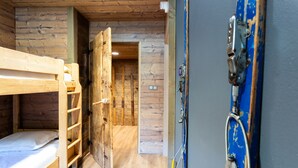 Une chambre avec un lit superposé en bois, une échelle, une porte donnant sur un couloir et un mur bleu orné d’un élément décoratif en métal.