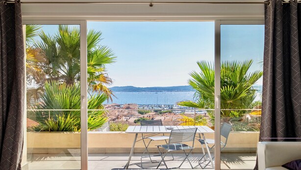 Een balkon met een tafel en stoelen, met uitzicht op een kustplaatsje en de zee.