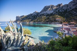 A coastal view with clear turquoise waters, rocky cliffs, and a building with red-tiled roofs. - BEACH & CALANQUES 300yd away, COSY HOUSE 10min from the heart of Marseille, Wifi (Marseille)