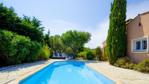 A rectangular swimming pool with a stone border, surrounded by lush greenery and a building with a window on the right. - Luxury villa with view of the putting green - Gulf of Saint-Tropez (Sainte-Maxime)
