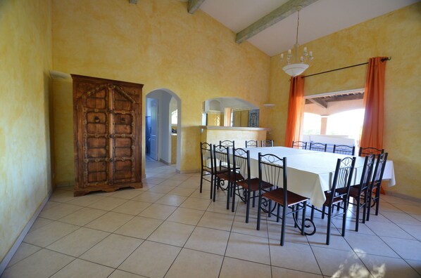 Un comedor con una mesa grande y sillas, una puerta de madera y piso de baldosas.