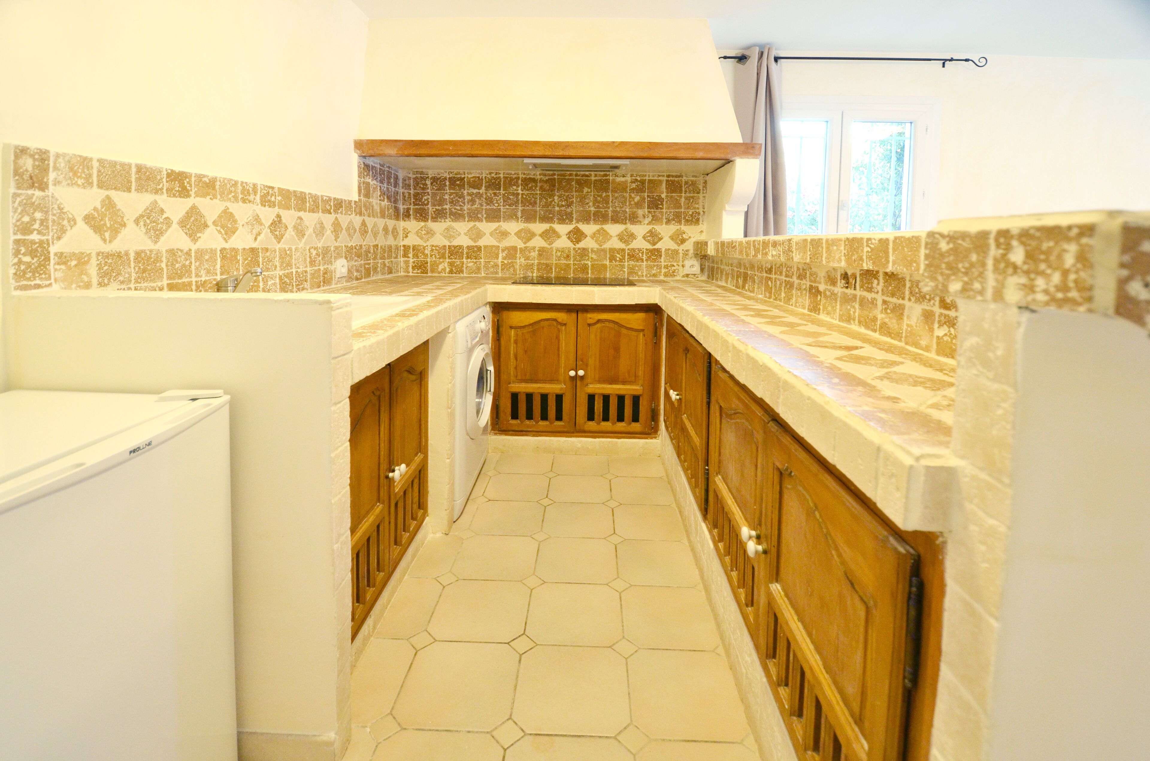 Une cuisine étroite avec des carreaux hexagonaux formant un motif, des armoires en bois et un réfrigérateur blanc.