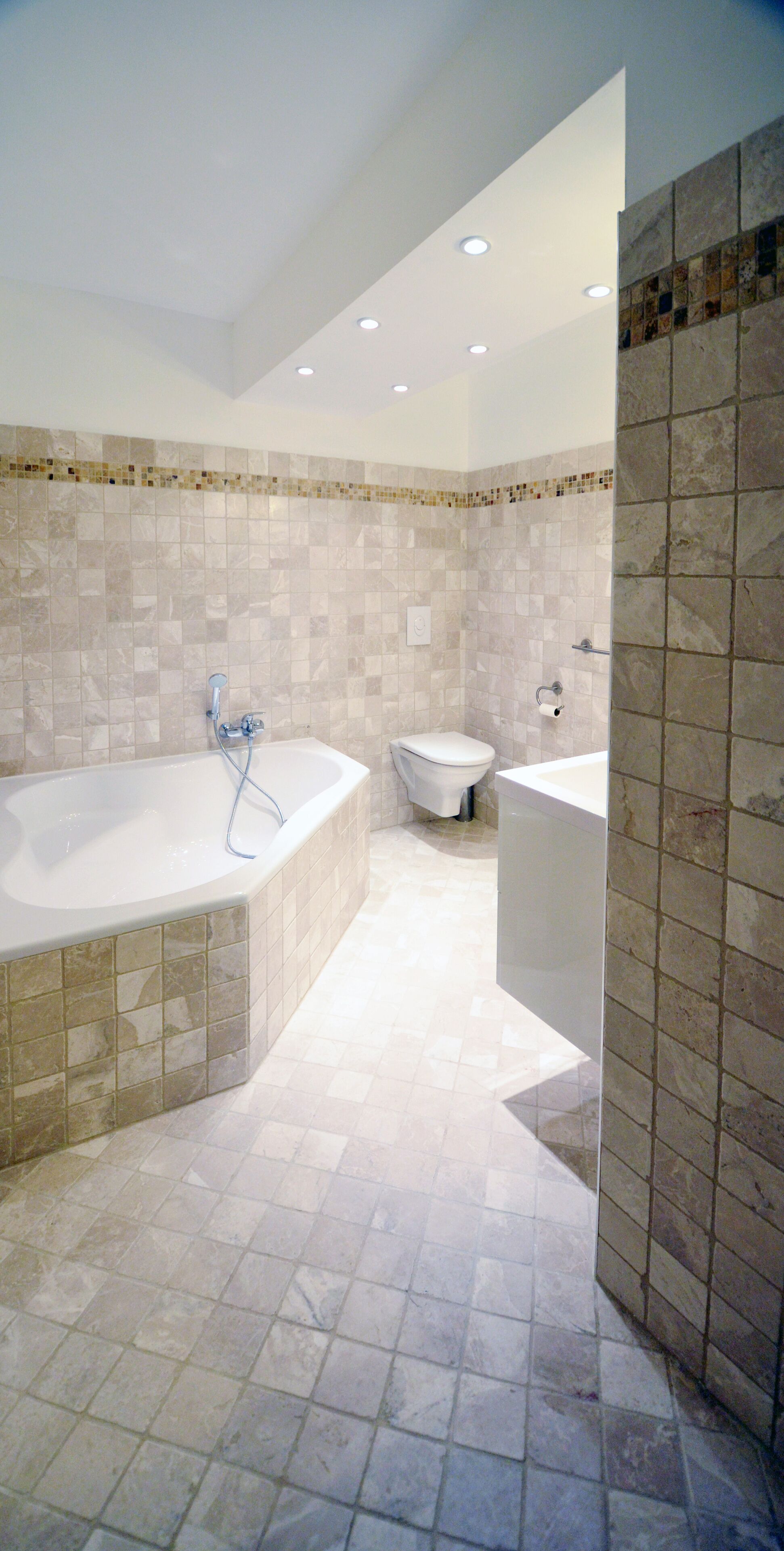 Une salle de bain moderne équipée d’une baignoire, de toilettes et d’un lavabo, avec des murs et un sol carrelés.