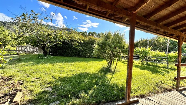 Un'area esterna riparata con un pavimento in legno, circondata da un prato e alberi.