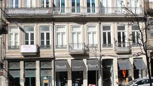 Un edificio de varios pisos con una fila de tiendas en la planta baja, incluyendo una farmacia y un restaurante.