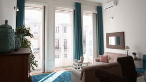 Una sala de estar con sofá, sillones, una mesa de centro y vistas amplias a través de ventanas con cortinas.