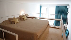 Un dormitorio con cama, almohadas, mesita de noche, lámpara, ventana con cortinas y vistas al exterior.