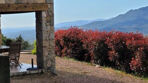 A stone-built outdoor seating area with a table and chairs, overlooking a mountainous landscape and a red flowering bush. - Dry stone cottage with outdoor spa, quietness guaranteed (Granace)