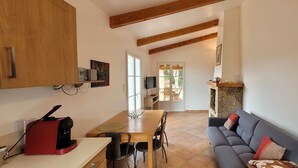 A modern kitchen with a coffee machine, a dining table with chairs, a grey sofa, and a stone fireplace. - Dry stone cottage with outdoor spa, quietness guaranteed (Granace)