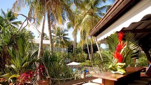 Un espacio al aire libre tropical con una mesa y sillas de madera, rodeado de abundante follaje y palmeras.