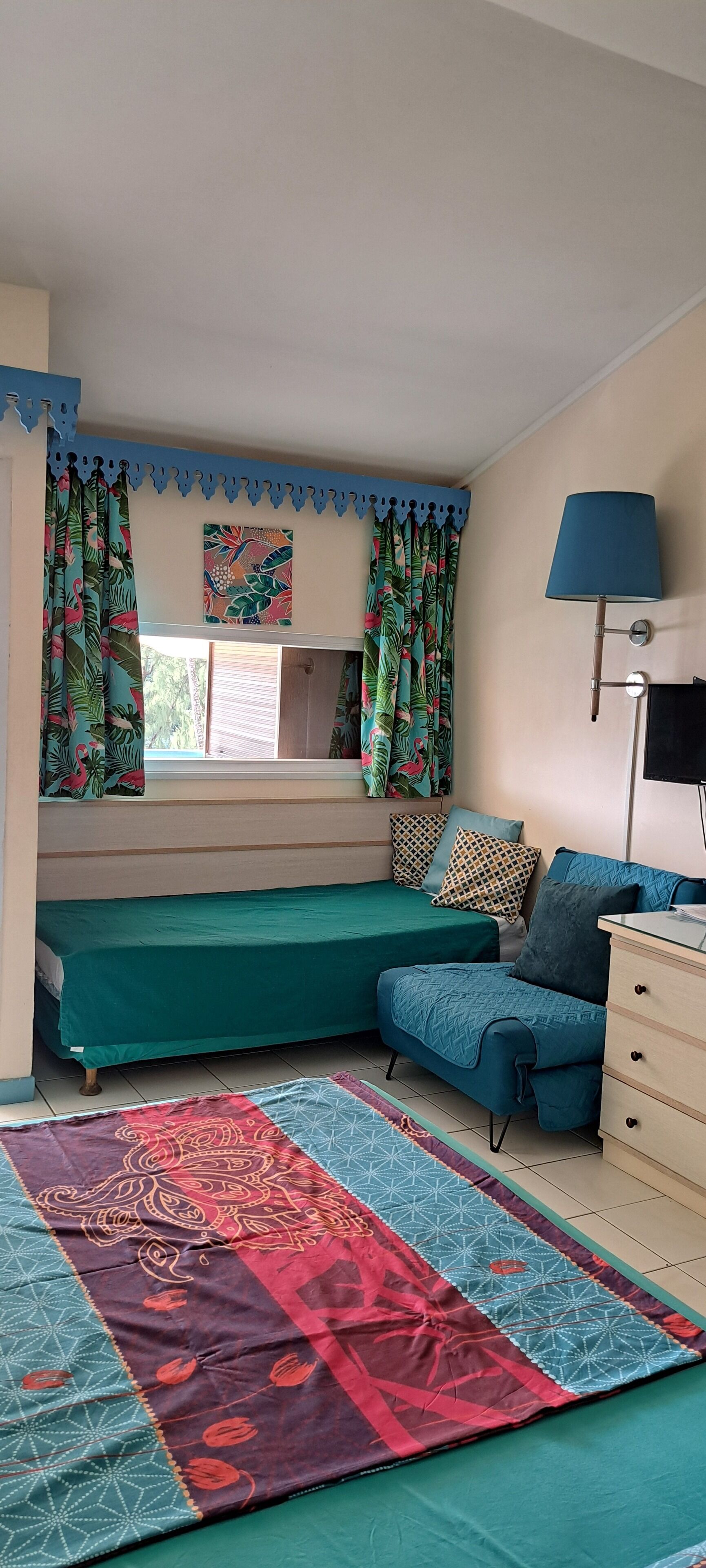 Een slaapkamer met twee bedden, een raam met gordijnen, een bedlampje en een kamerkleed met dessin.
