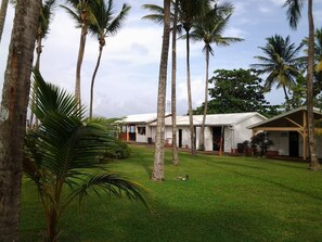 A bungalow-style building with a covered porch, surrounded by palm trees and a well-maintained lawn. - FUNCTIONAL STUDIO HOTEL CARAYOU SPA BEACH SWIMMING POOLS (Les Trois-Îlets)