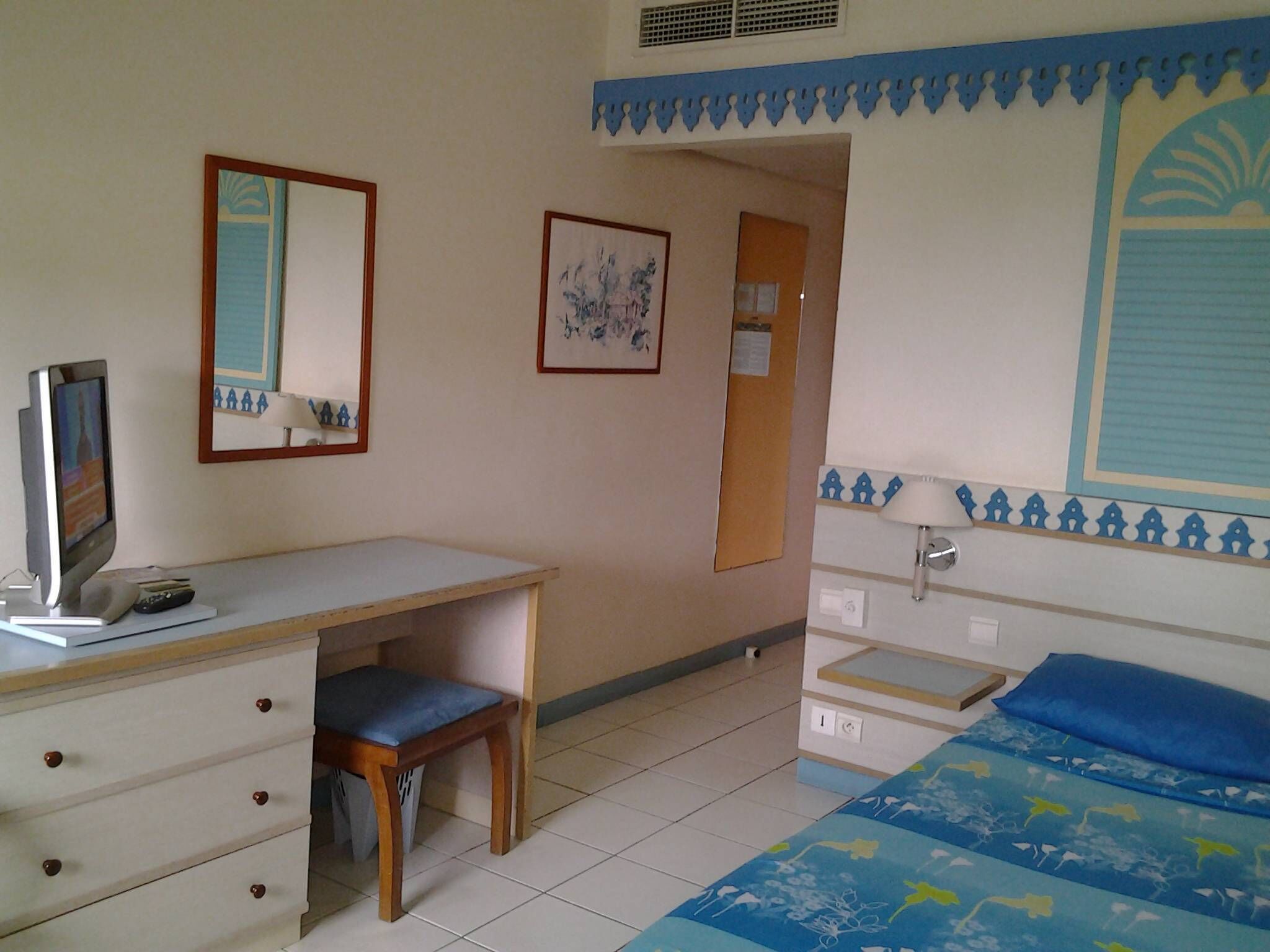 A hotel room with a desk, chair, bed, and a wall-mounted TV.