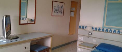 A hotel room with a desk, chair, bed, and a wall-mounted TV.