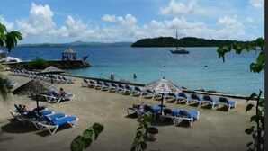 Una playa con sillas de playa y sombrillas, una pequeña cabaña y un bote en el agua.