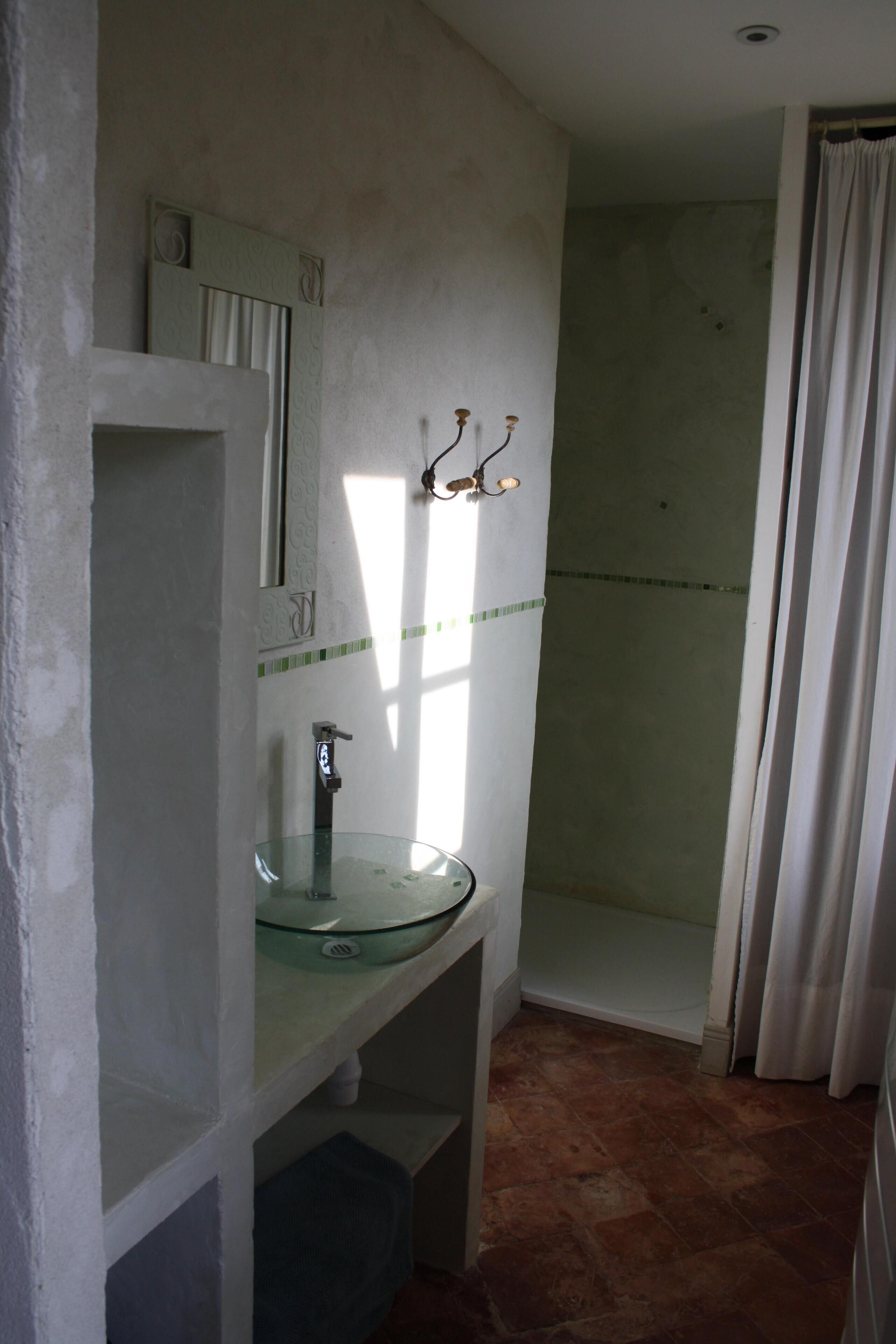 A bathroom with a glass sink, a shower, and a mirror.