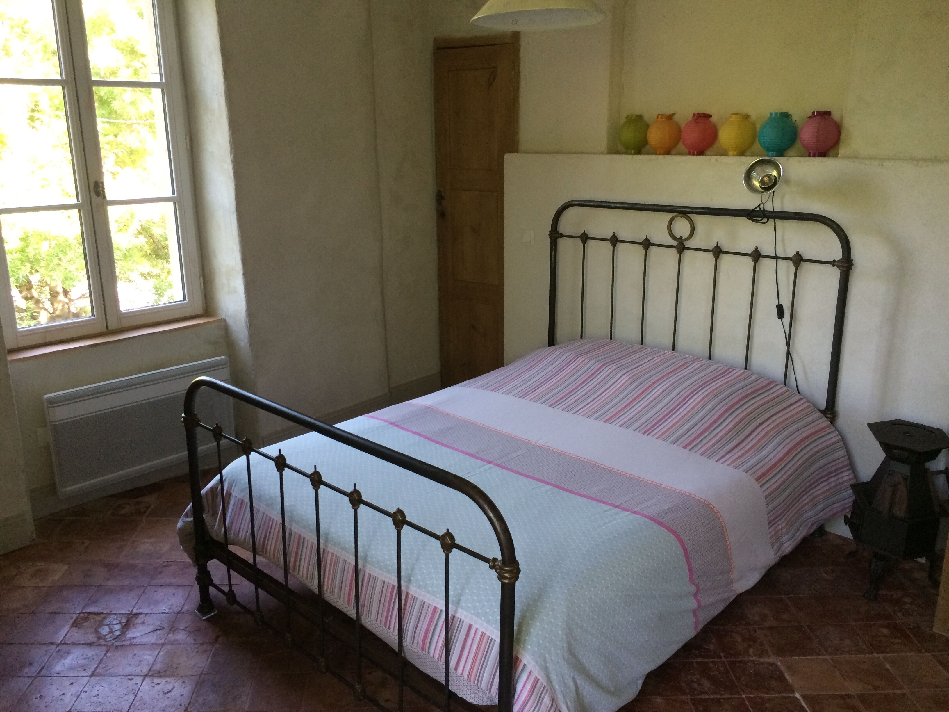 A room with a bed, a window, a radiator, and a shelf with colorful vases.