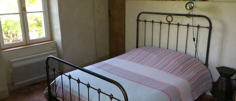 A room with a bed, a window, a radiator, and a shelf with colorful vases.