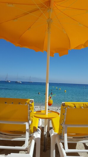 A beach setting with yellow chairs and an umbrella, a clear blue sea, and boats in the background.