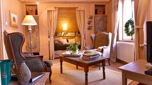 Una habitación acogedora con suelo de madera, un sofá, una silla, una mesa con libros y un florero, y una ventana con cortinas.