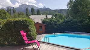 Una piscina con muelle de madera, una silla rosa y una cabaña de madera pequeña.