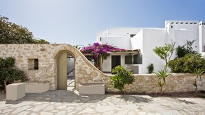 A stone pathway leading to a white building with a stone archway and a small garden with purple flowers.