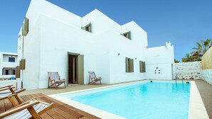 A modern white building with a swimming pool, wooden deck, and lounge chairs.