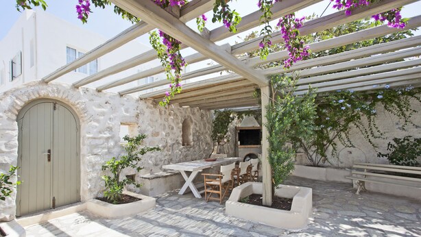 A stone patio with a pergola, outdoor seating, and a stone wall.