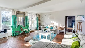 A spacious living room with a large window, a white sofa, green chairs, and a coffee table.