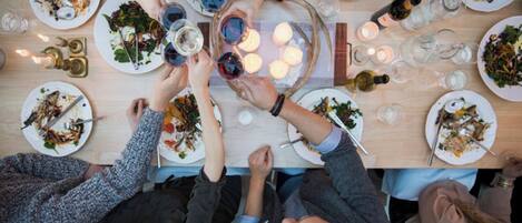 Un grupo de personas sentadas alrededor de una mesa con platos de comida, copas de vino y velas, evocando un ambiente de cena social.