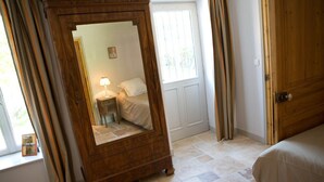 A bedroom with a wooden wardrobe, a bed, a nightstand with a lamp, and a window with curtains.