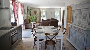 A spacious dining area with a table set for four, flanked by a kitchen and a living area with a sofa and a plant.