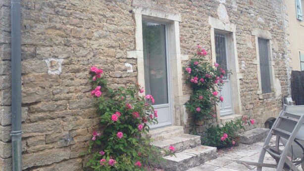 A stone building with two windows and a door, surrounded by pink flowers.