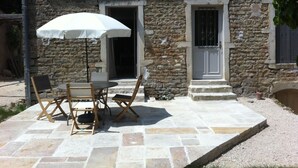 A stone building with a patio area featuring a table and chairs, an umbrella, and a door.