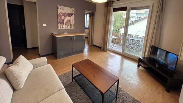 Ein modernes Wohnzimmer mit Sofa, Couchtisch, Fernseher und einem Balkon mit Blick.