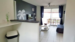 A compact living space with a kitchen area, a dining table, and a balcony with a view.