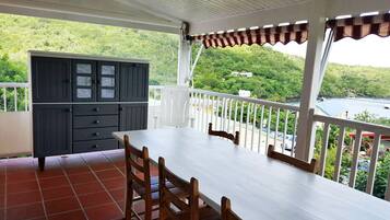 A balcony with a white table and chairs, a grey cabinet, and a view of a lush green landscape and water.