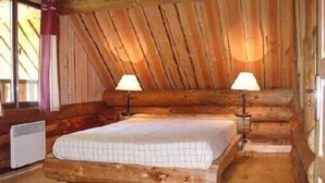 Ein Schlafzimmer in einer Blockhütte mit einem Bett, zwei Nachttischlampen und einer Heizung.
