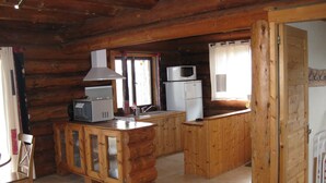 Ein Interieur einer Holzhütte mit Küchenbereich, einschließlich einer Mikrowelle, eines Kühlschranks und einem Holzkabinett mit Glastür.